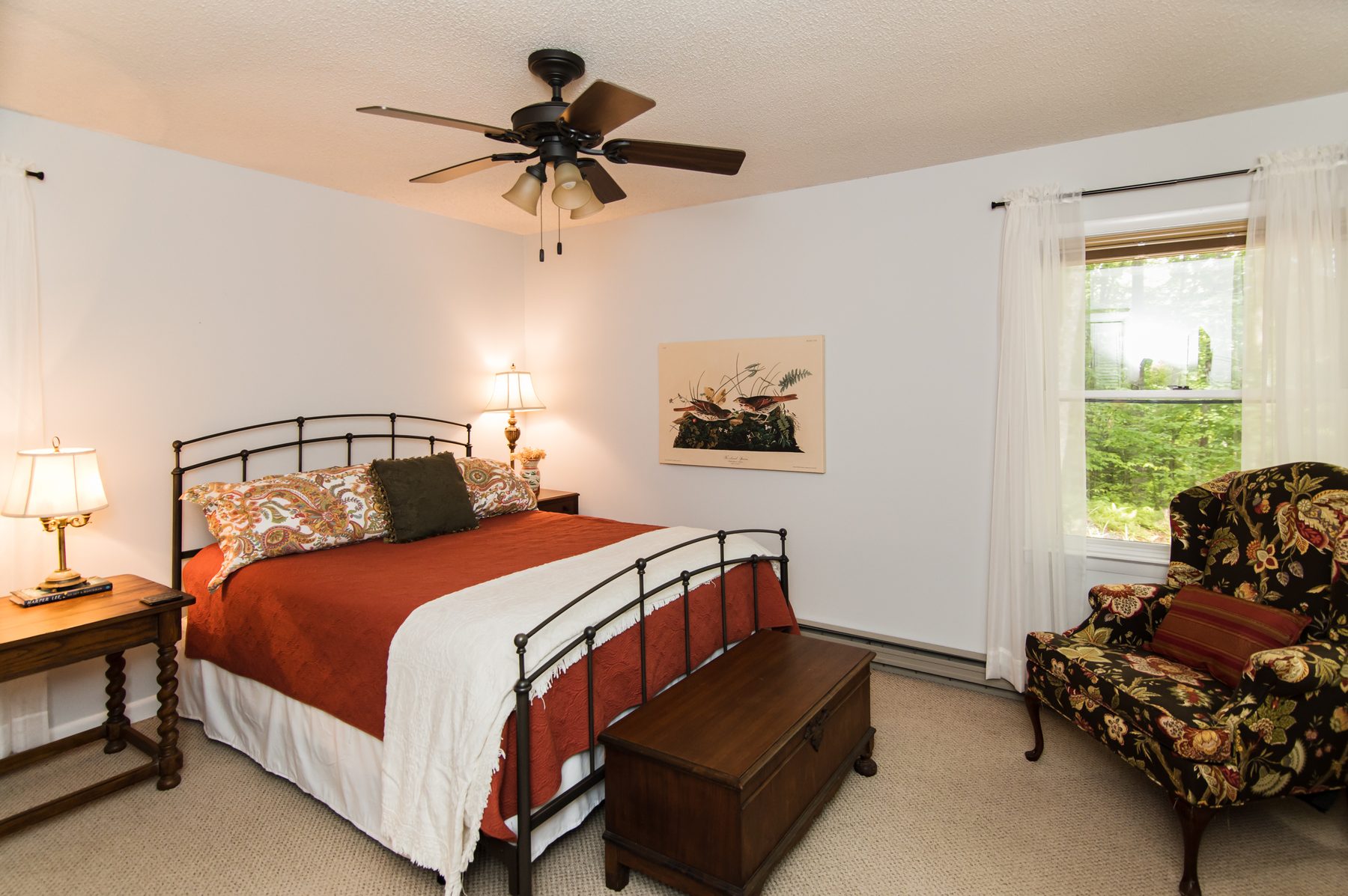 Queen bedroom with an iron bed, reading chair and a forest-view window