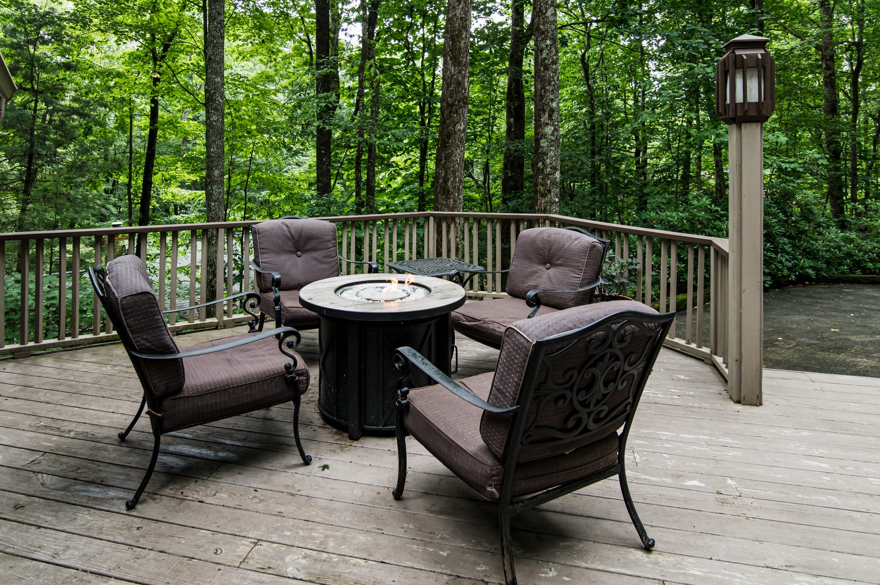 Cushioned chairs around a gas firepit on the back deck surrounded by trees