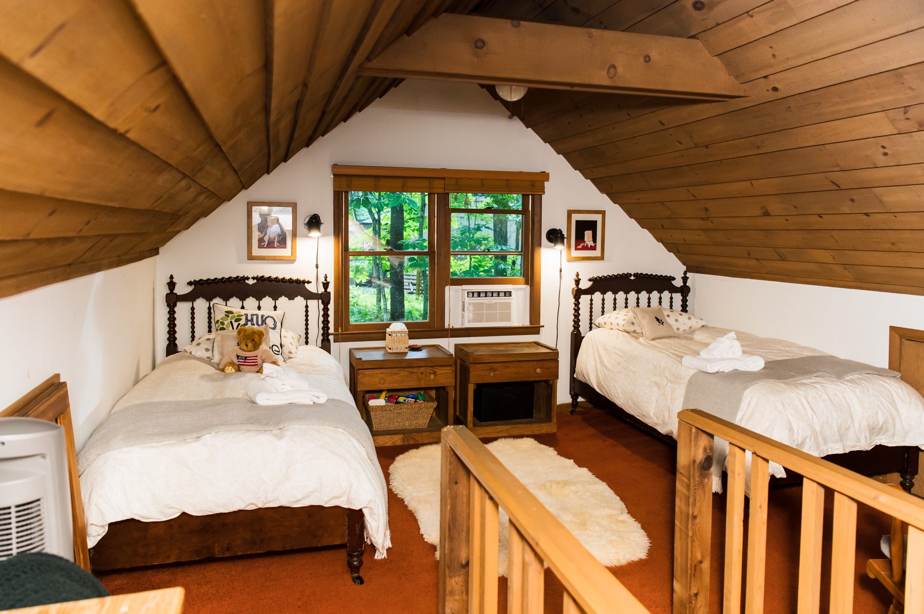 Loft with two twin beds under a beamed wood ceiling and a forest-view window