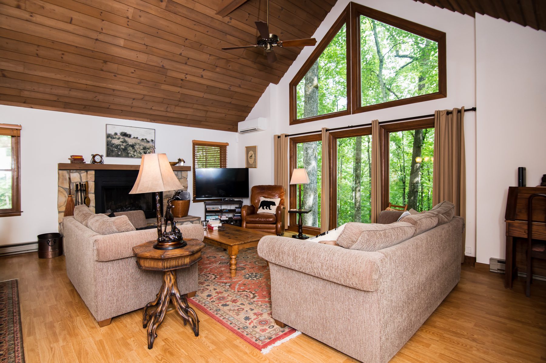 Living room with stone fireplace, leather chair and two-story windows onto the forest