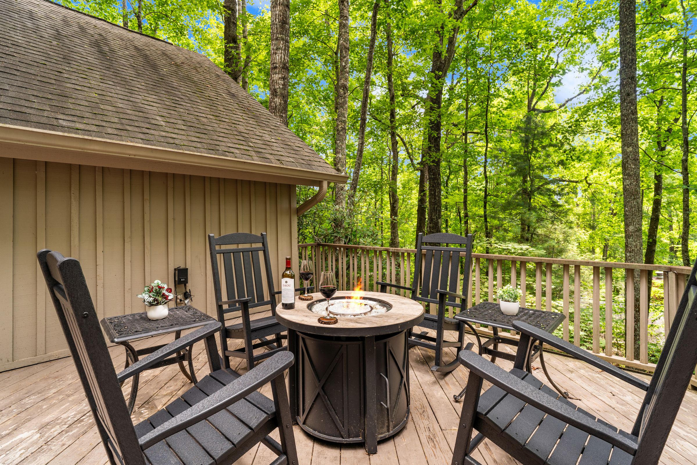 Rocking chairs around the tabletop firepit on the front deck, under tall trees