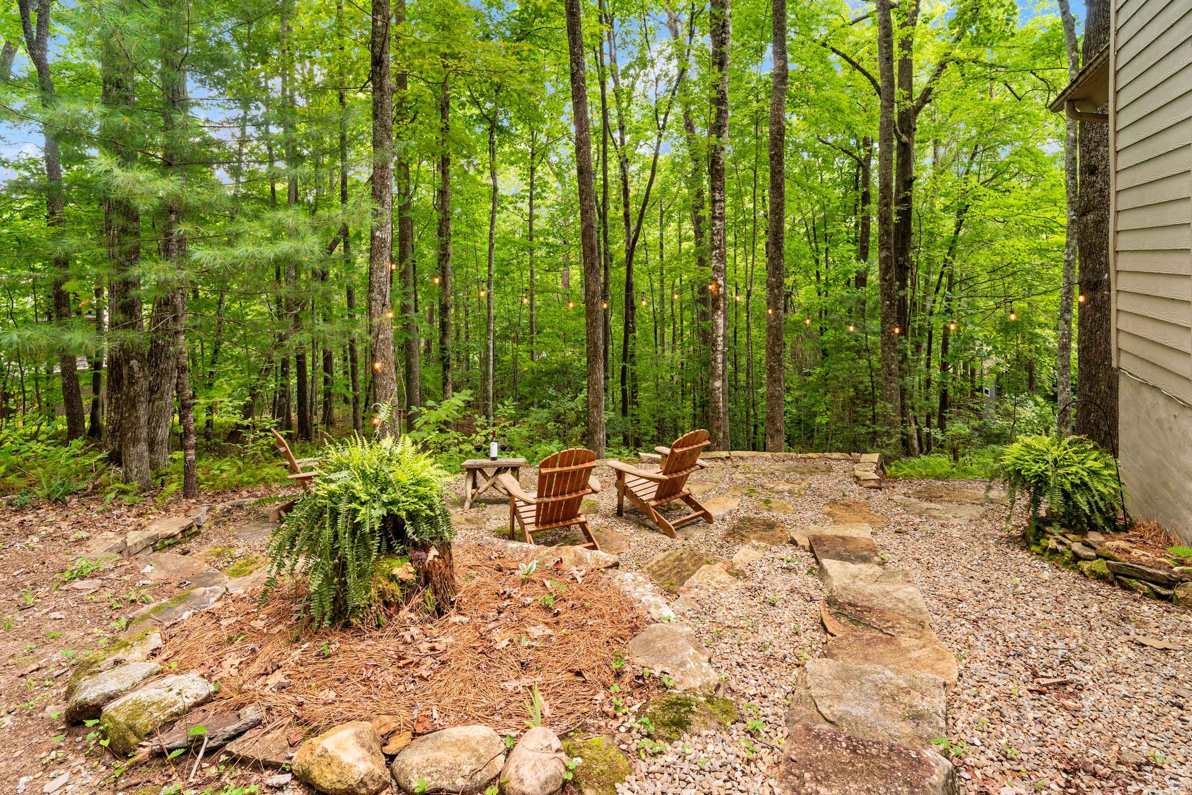 Adirondack chairs around a stone firepit in the woods beside the cottage