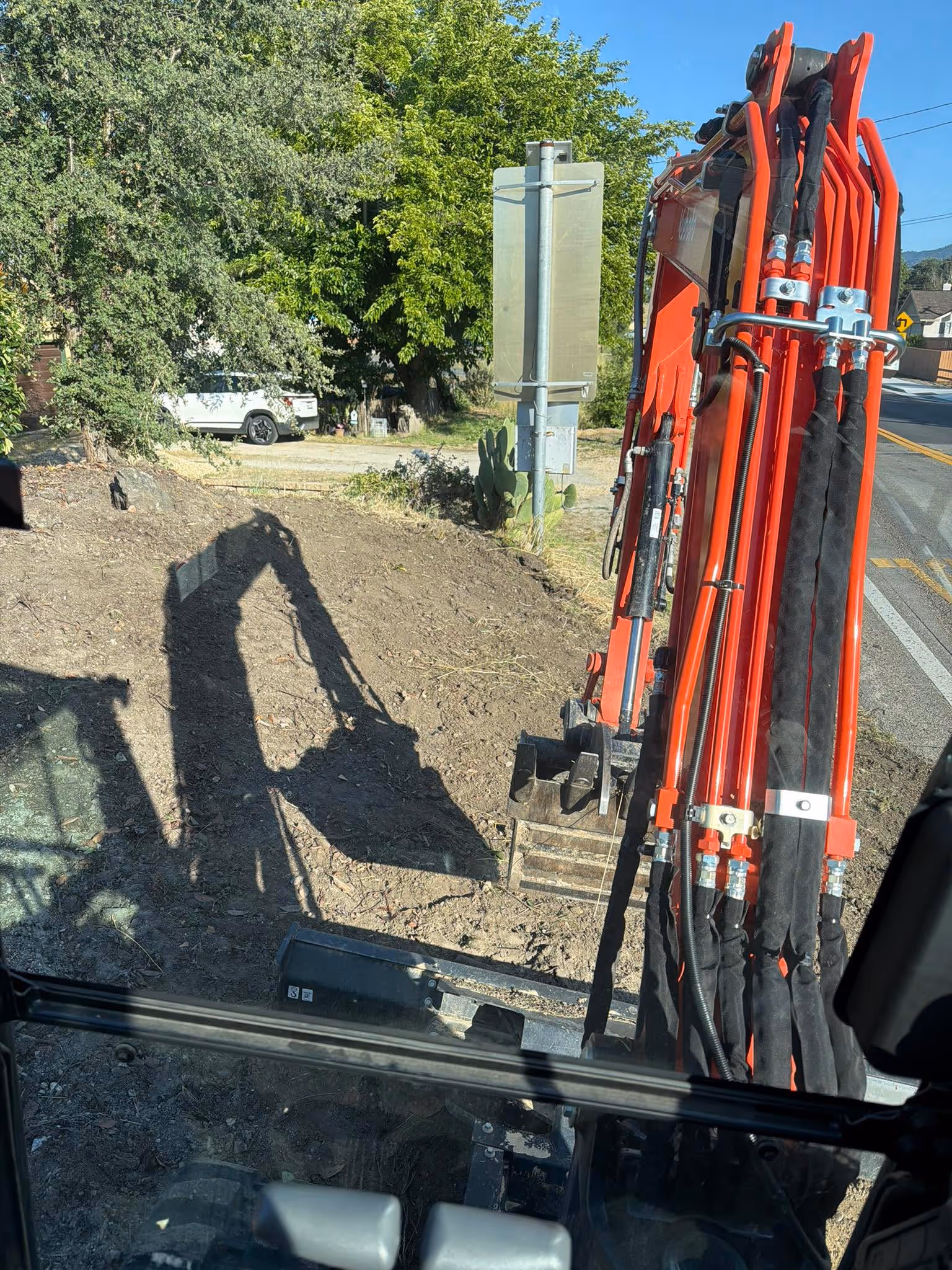 Orange excavator performing roadside dirt removal, demonstrating heavy equipment land clearing in SLO County.