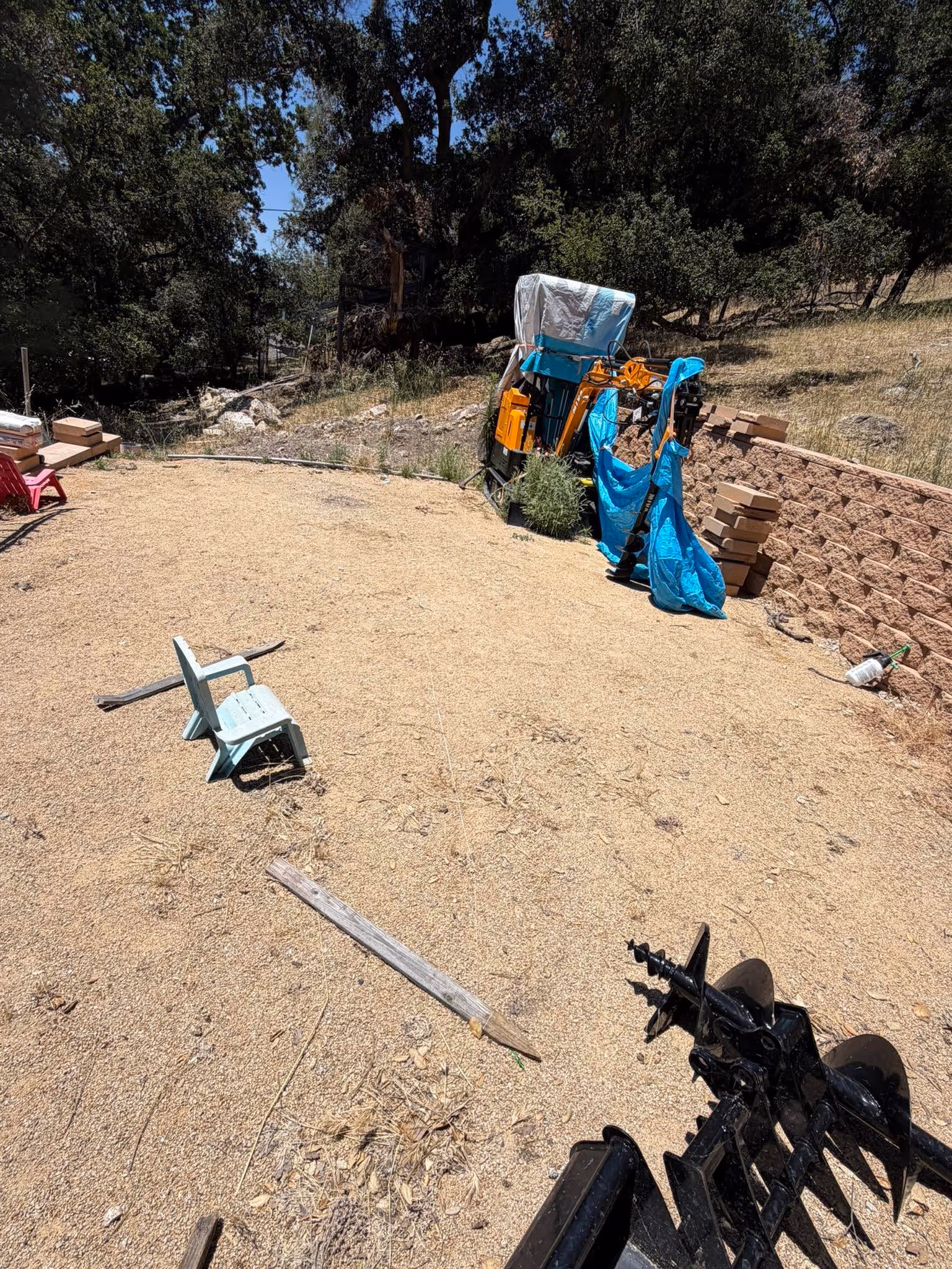 Construction equipment including an auger drill attachment and a freshly graded dirt driveway next to a metal residential gate, highlighting site preparation and grading services in SLO County.