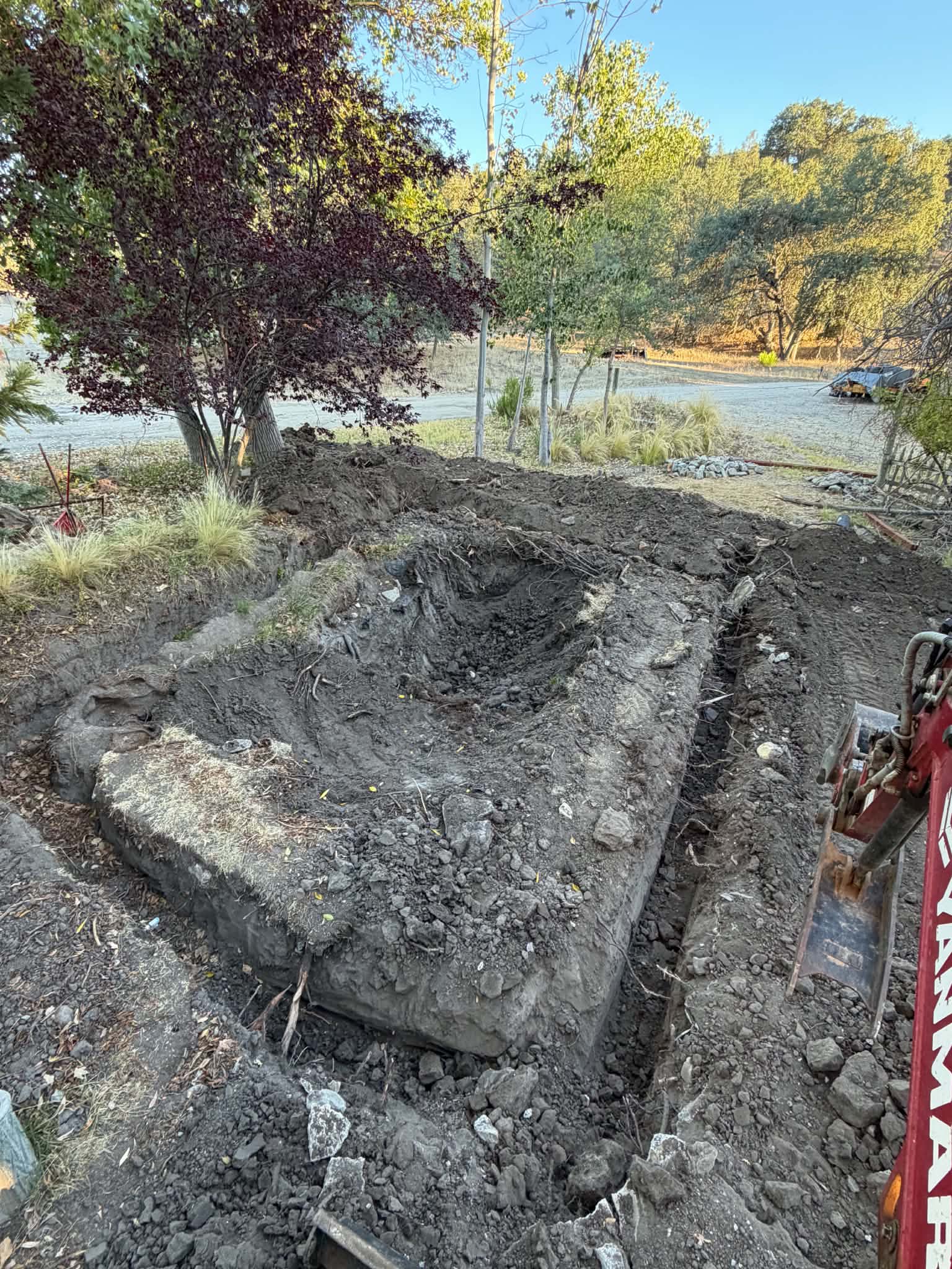 Construction equipment including an auger drill attachment and a freshly graded dirt driveway next to a metal residential gate, highlighting site preparation and grading services in Templeton.