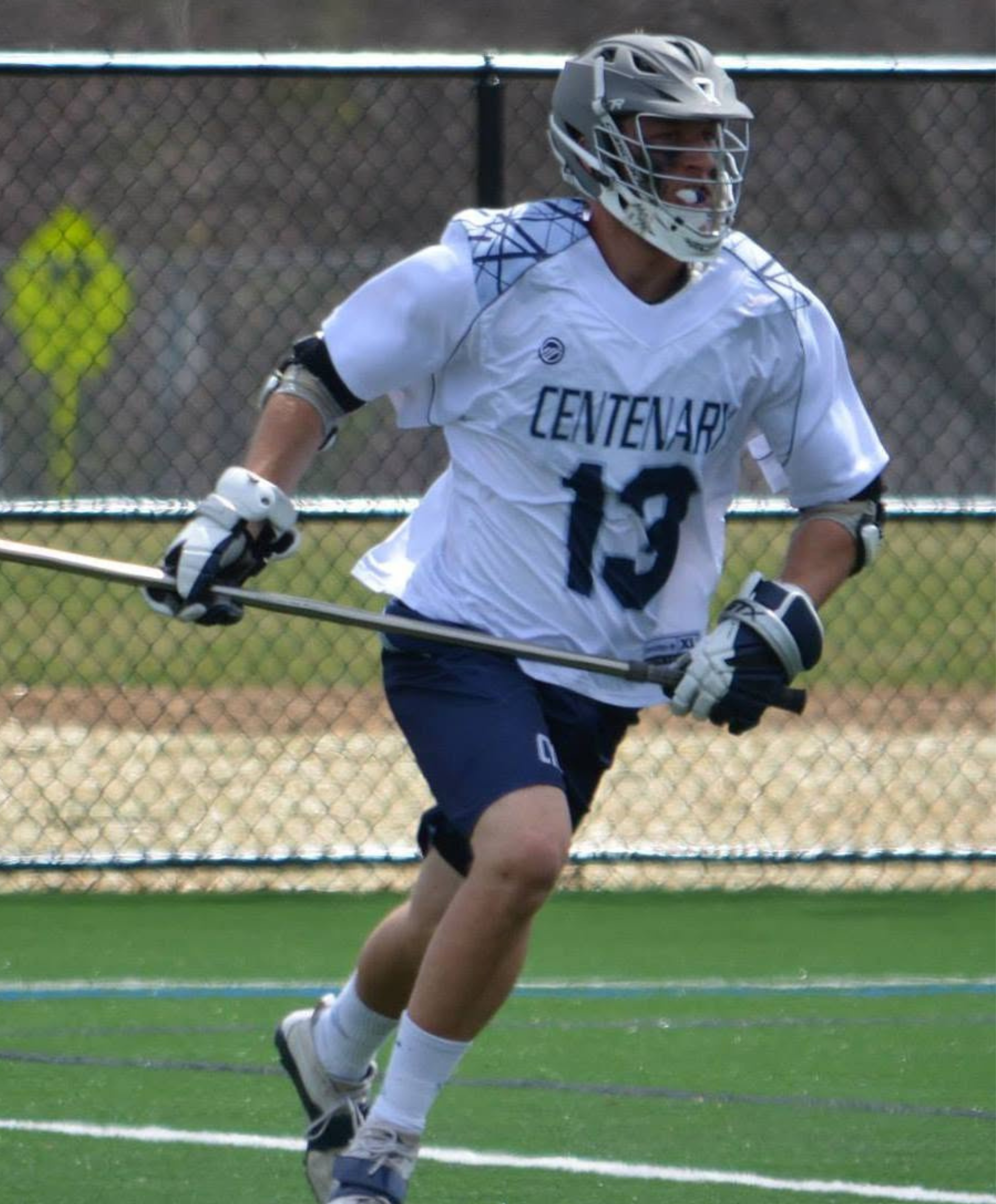 Lacrosse player wearing Centenary jersey number 13 running on a field with a lacrosse stick.