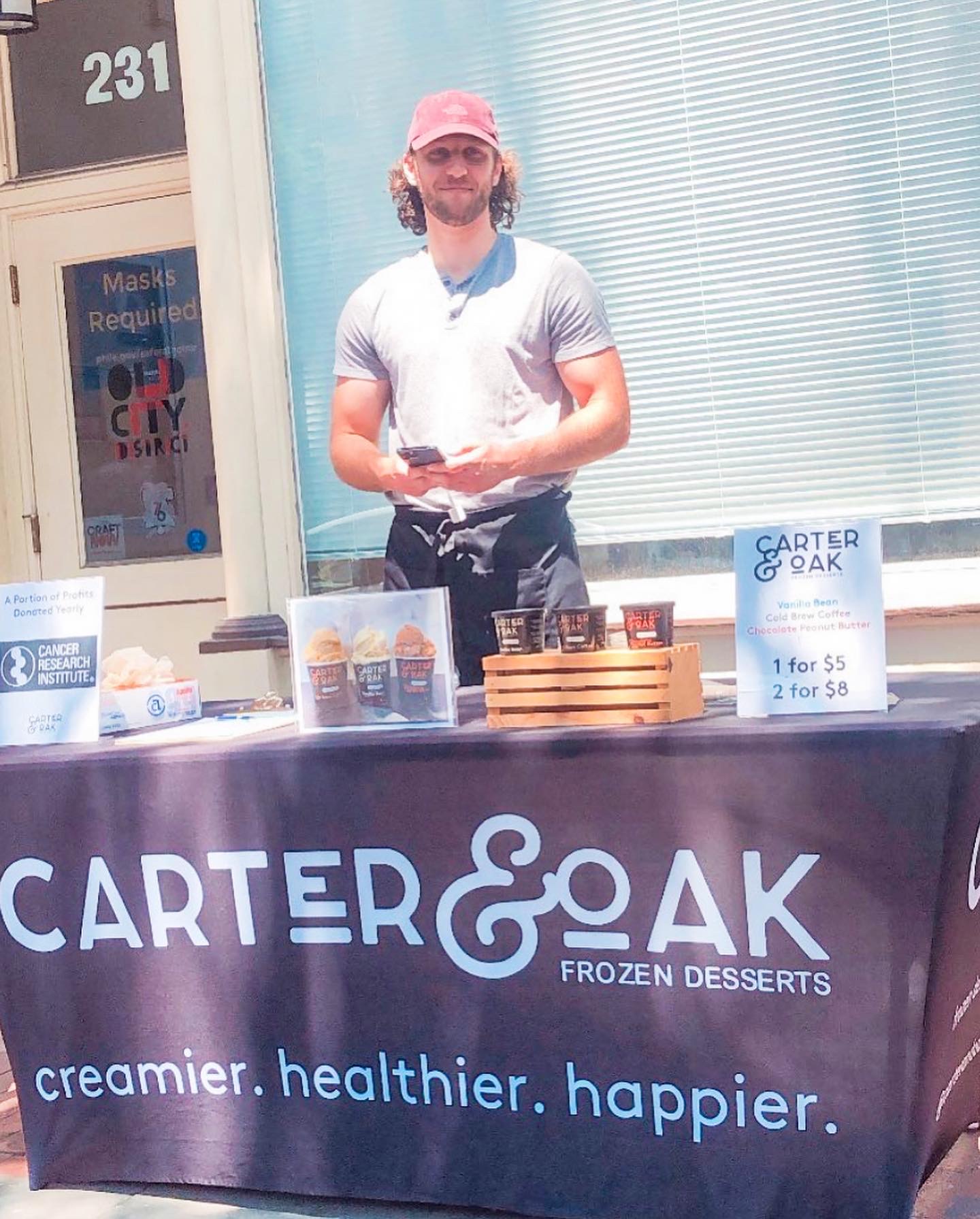 Man standing behind a Carter & Oak Frozen Desserts table with product samples and signage outdoors.