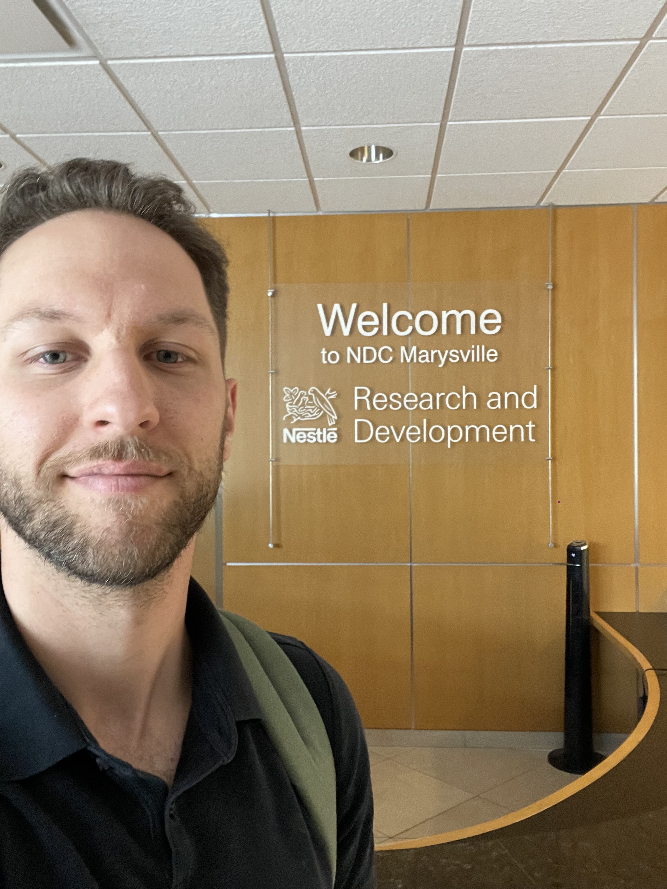 Man with beard and backpack in front of a wall sign saying Welcome to NDC Marysville Research and Development.