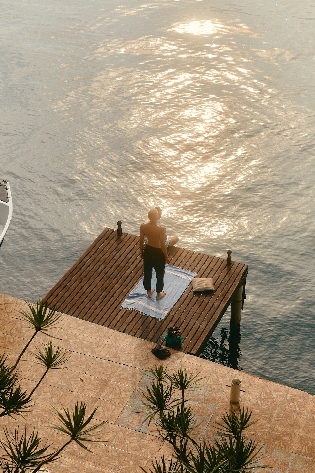Person standing on wooden dock over calm water reflecting sunlight in the evening.
