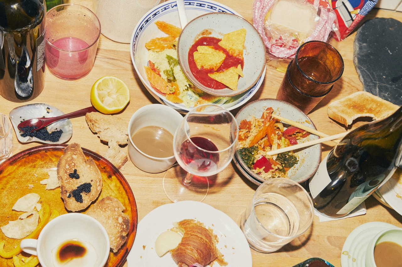 Overhead view of a messy wooden table with various dishes, drinks, and food remnants.
