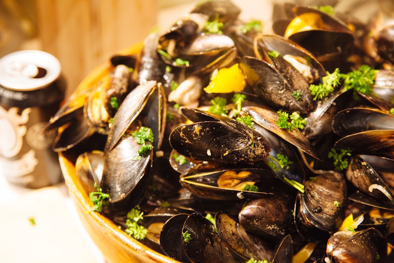 Close-up of cooked mussels garnished with parsley in a bowl with a can in the background.