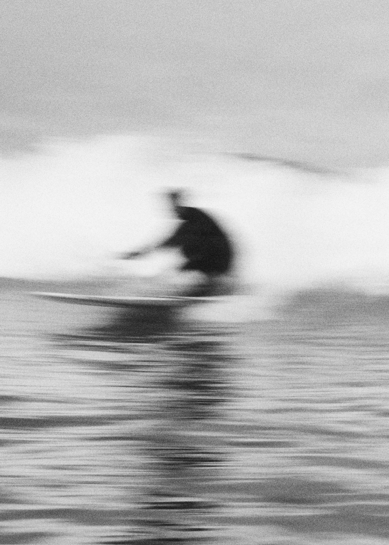 Blurred black and white image of a person surfing on a wave in the ocean.