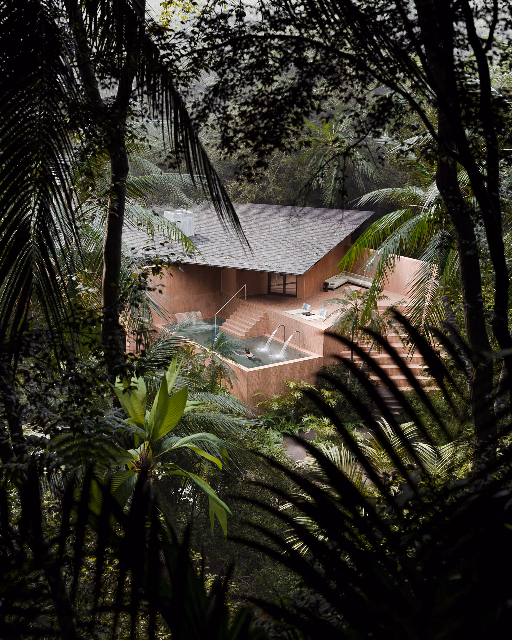 A pink sand-colored building with outdoor Thalassotherapy pool is seen through lush tropical forest vegetation.
