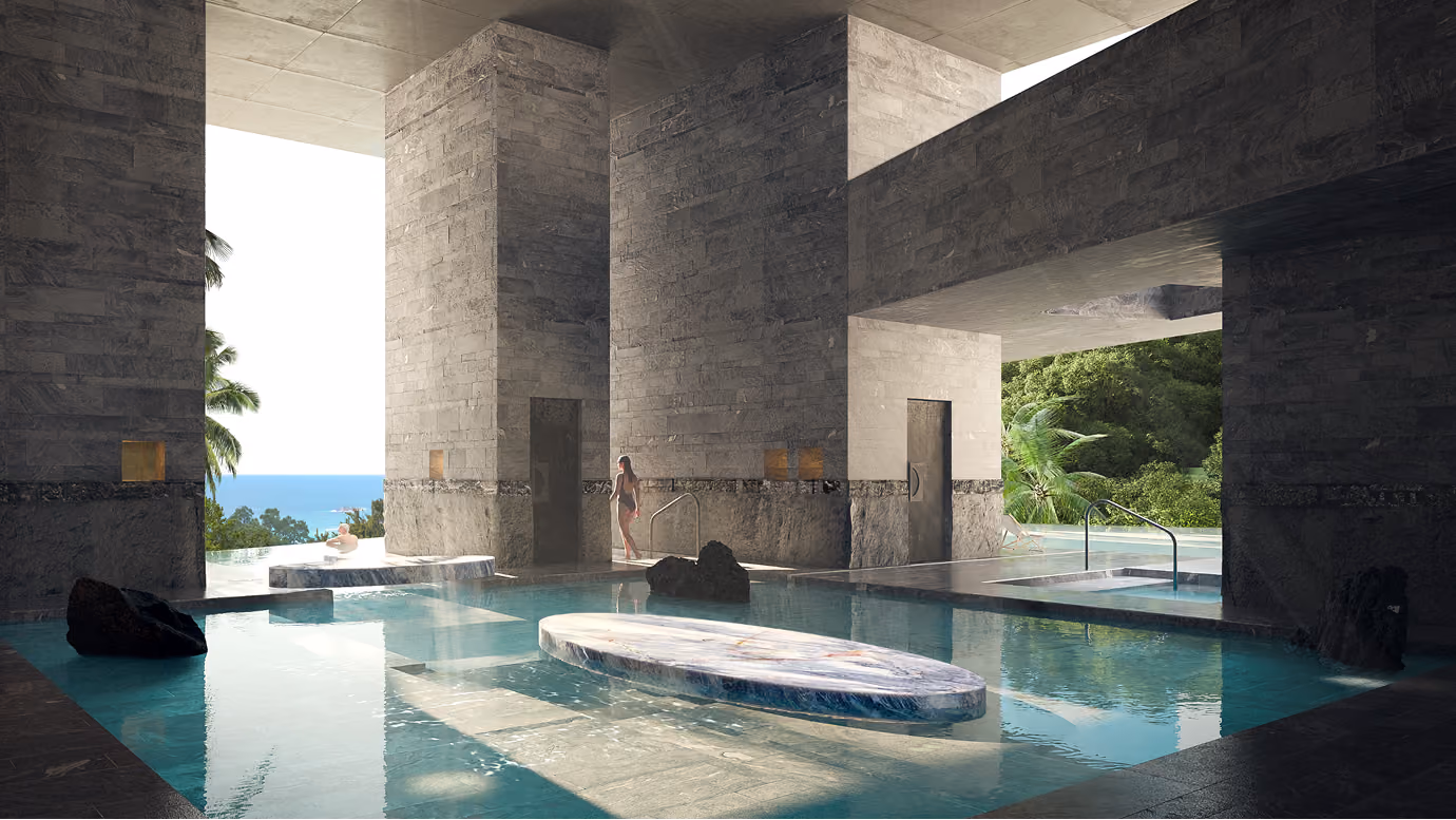 Modern indoor pool with stone walls, elevated marble platform, sunken boulders, and ocean and jungle views in the background.
