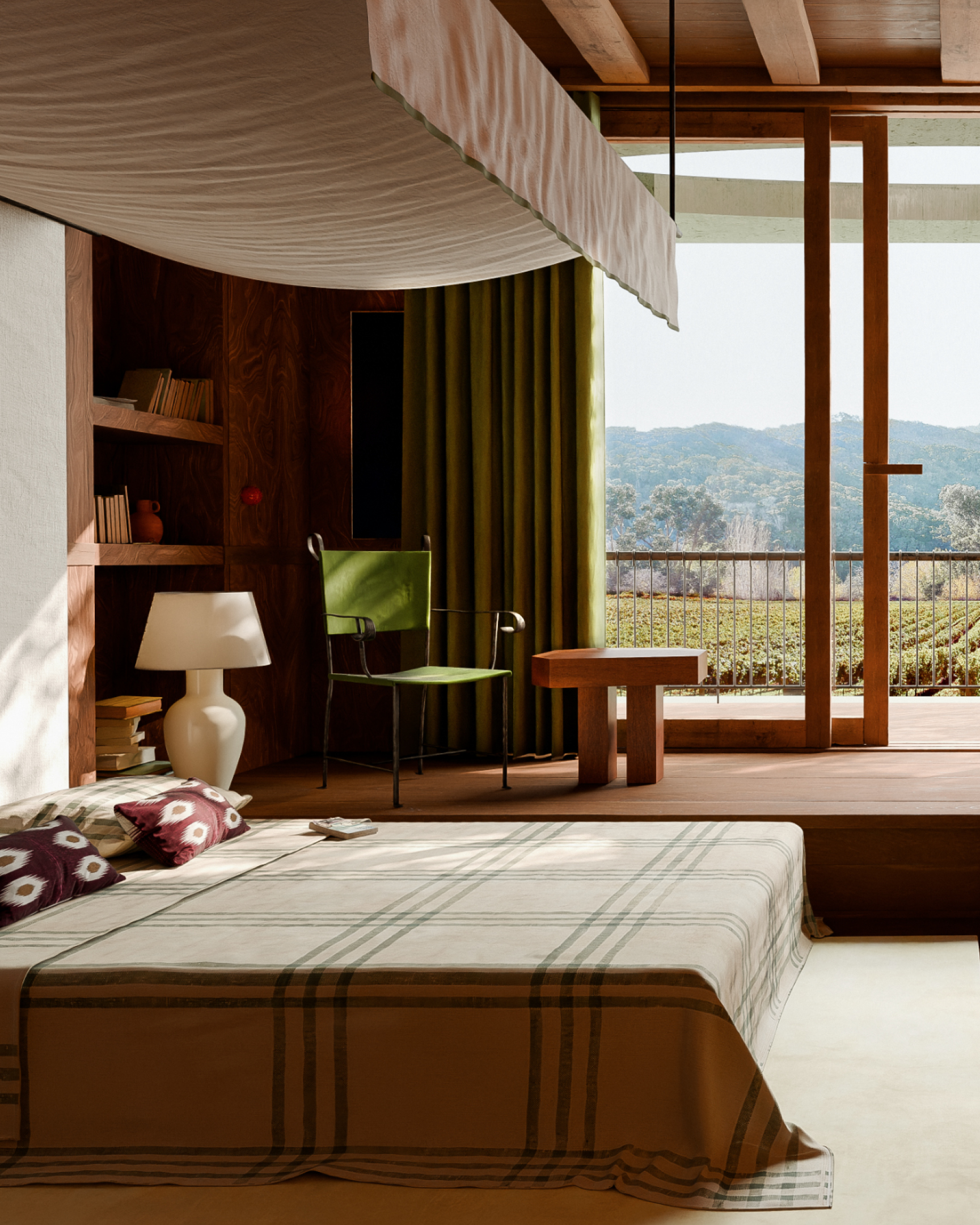 Cozy bedroom with green curtains, a chair, lamp, bookshelves, and a large window overlooking mountains.