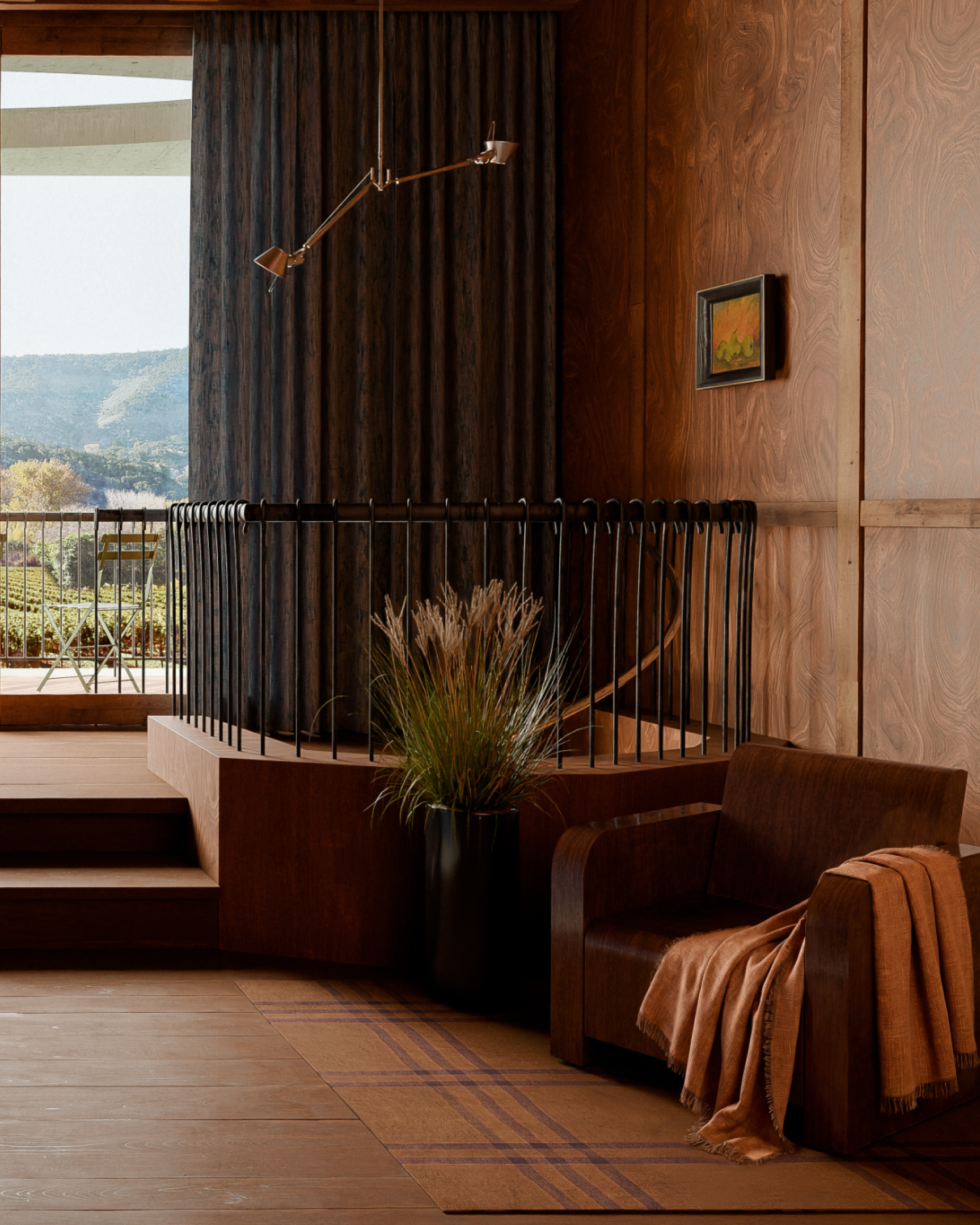 Modern cozy room with brown armchair, blanket, potted grass, and balcony overlooking green hills.