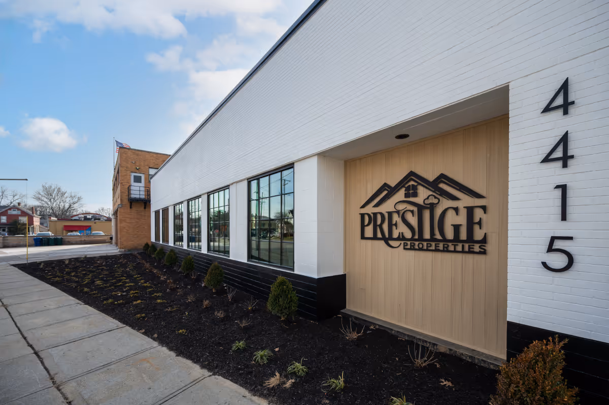 Modern white building with black trim and large windows, Prestige Properties sign, and address number 4415.
