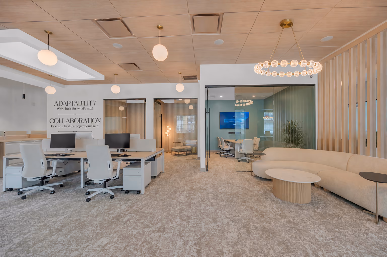 Modern office with white desks, chairs, meeting rooms, and beige curved sofa with round tables.