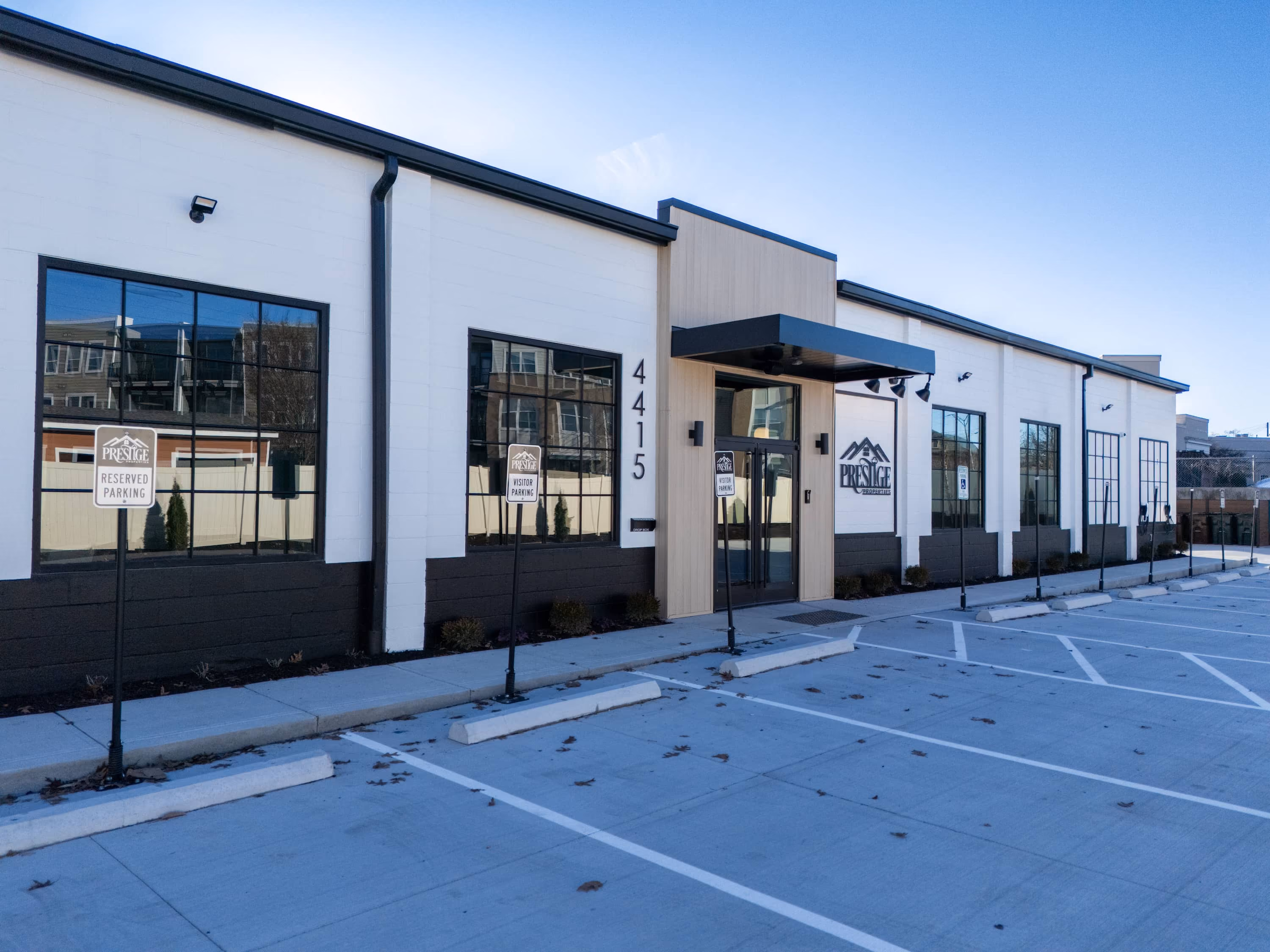 Exterior of Prestige Properties office with reserved and visitor parking signs in empty parking lot.