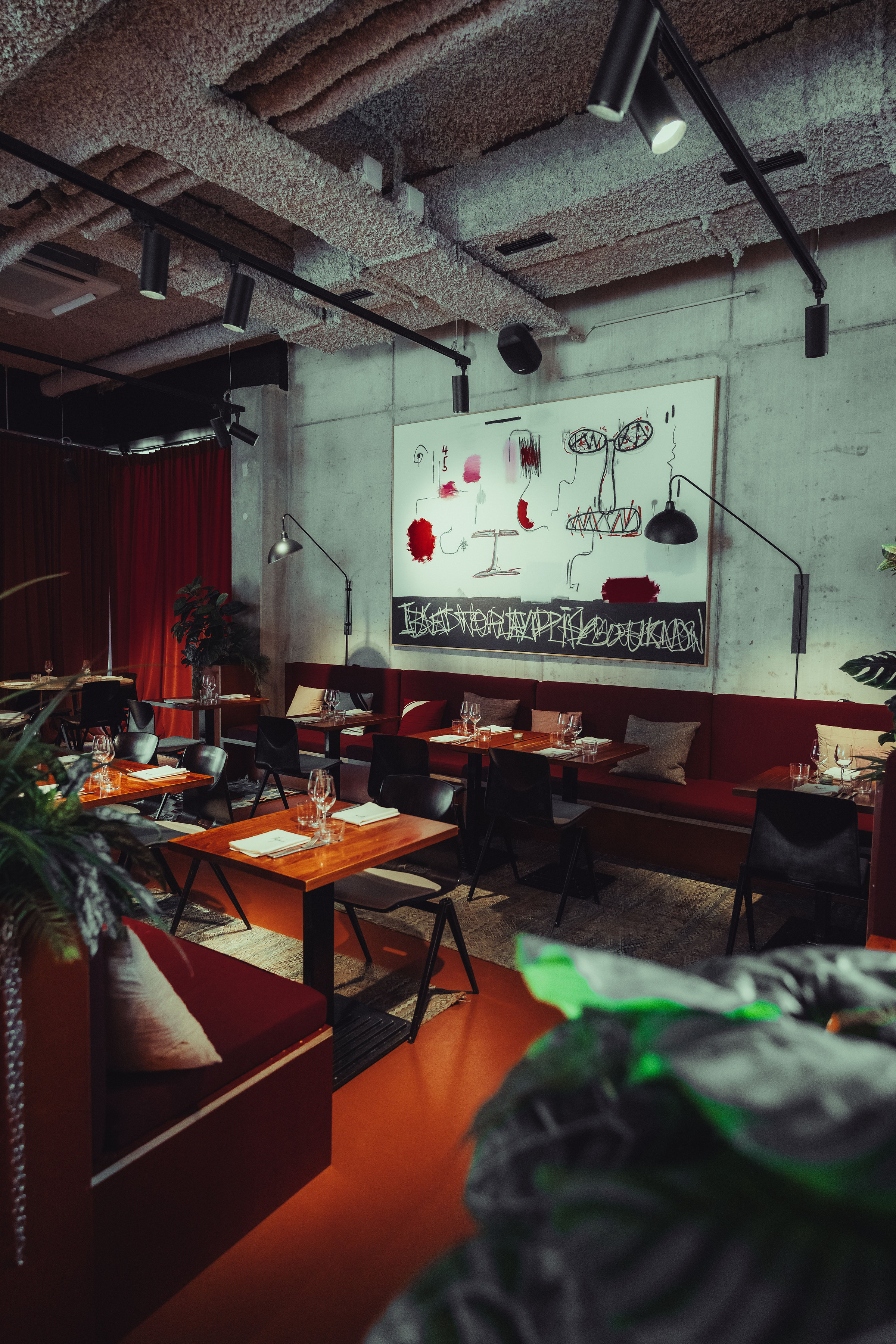 Salle de restaurant dressée avec grande peinture murale, banquettes rouges et tables en bois