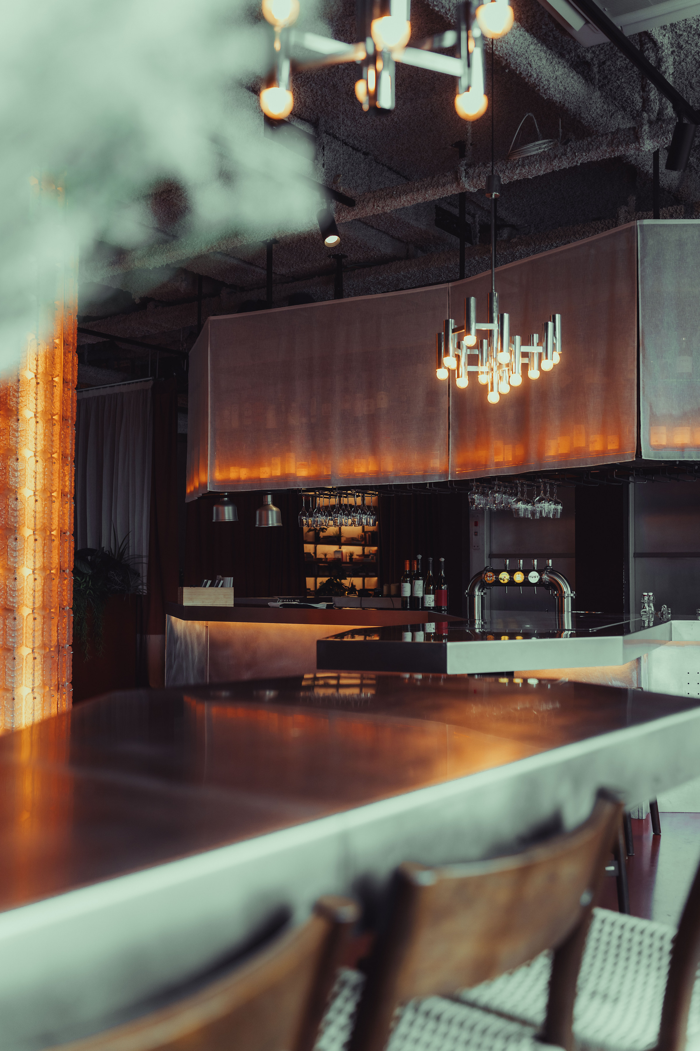 Bar éclairé par un lustre design, comptoir en acier et lumières chaudes