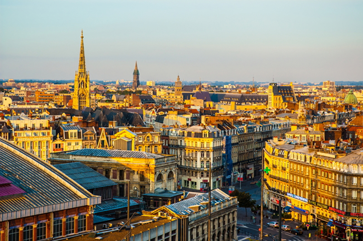 Vue panoramique de la ville avec des bâtiments anciens sous une lumière dorée au coucher du soleil.