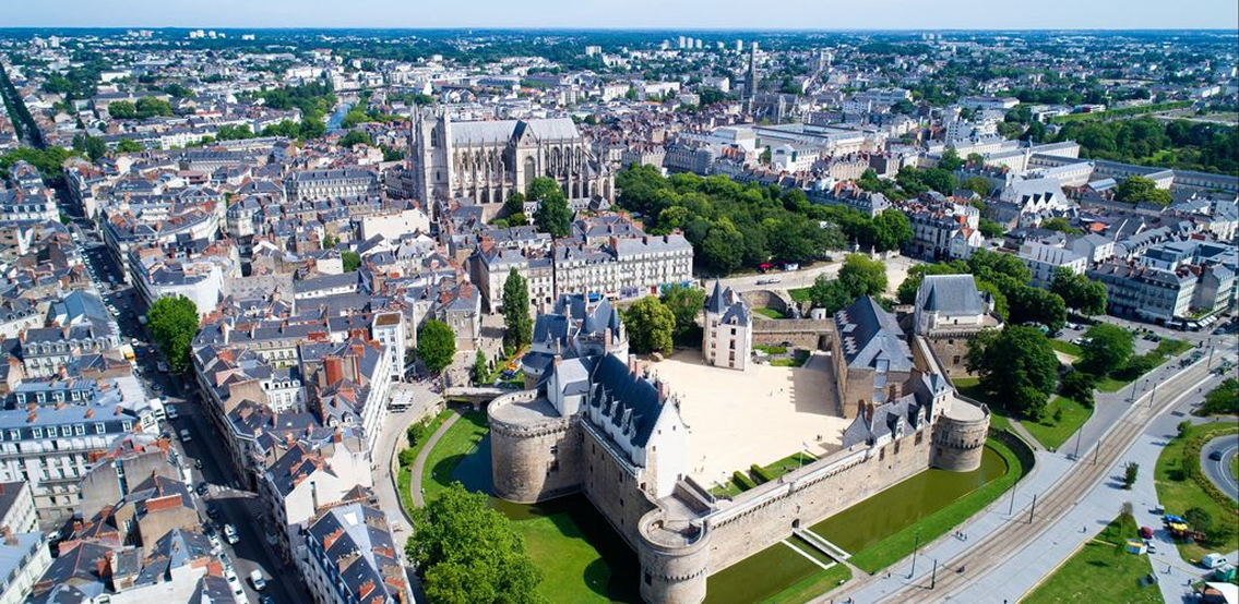 Vue aérienne du château des ducs de Bretagne à Nantes entouré par un fossé et des bâtiments historiques.