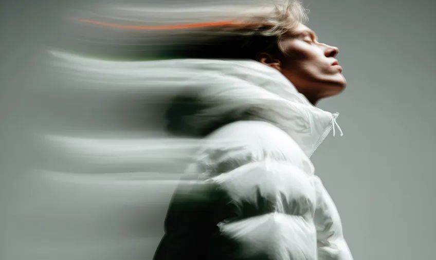 Side profile of a person in a white puffer jacket with blurred motion trailing from their head and shoulders.