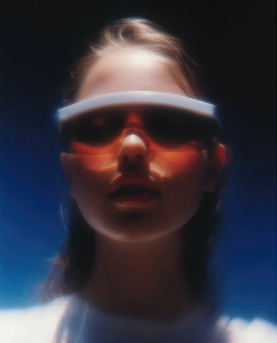 Close-up of a person wearing futuristic orange visor glasses against a dark blue background.