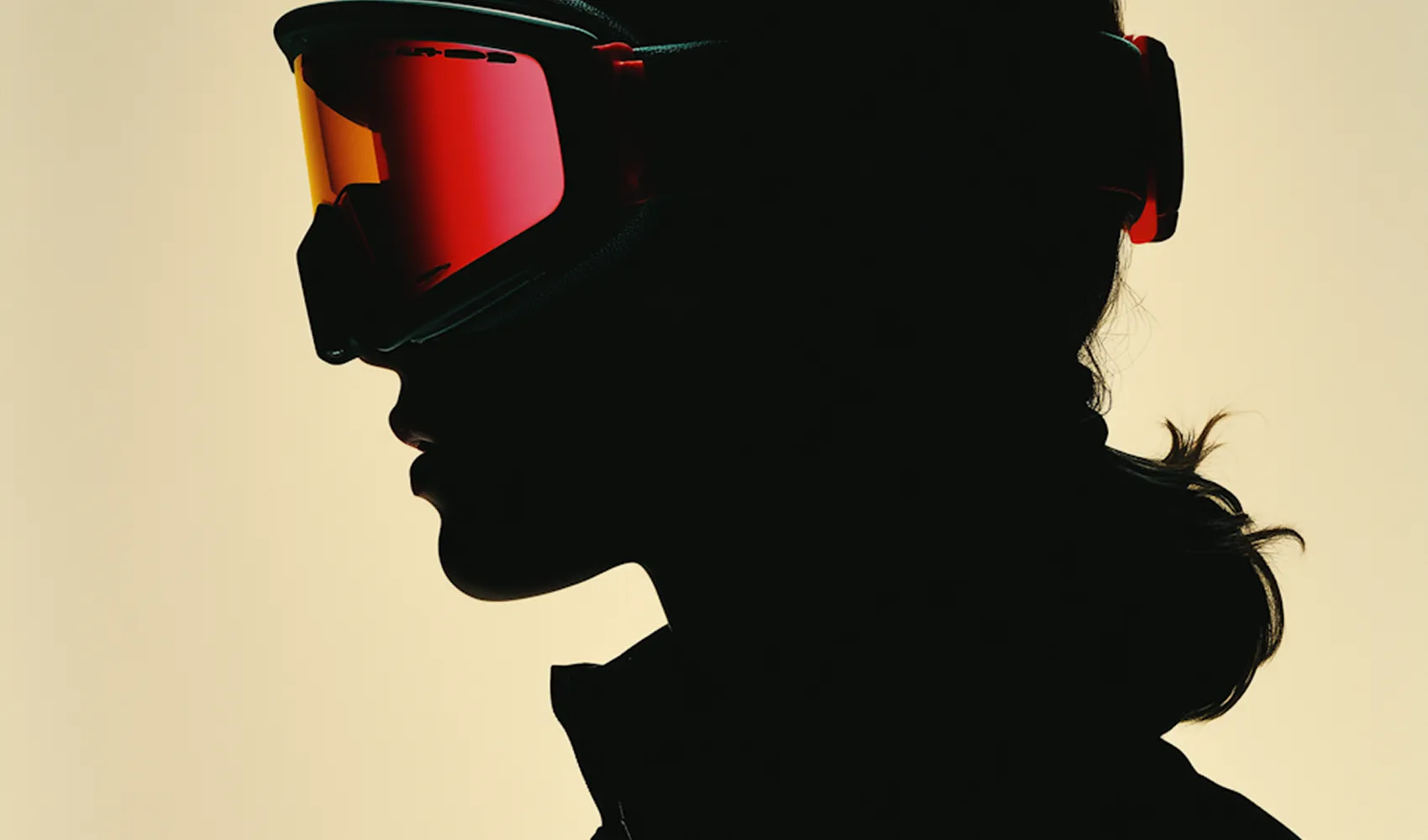 Silhouette of a person wearing red ski goggles and a jacket against a light background.