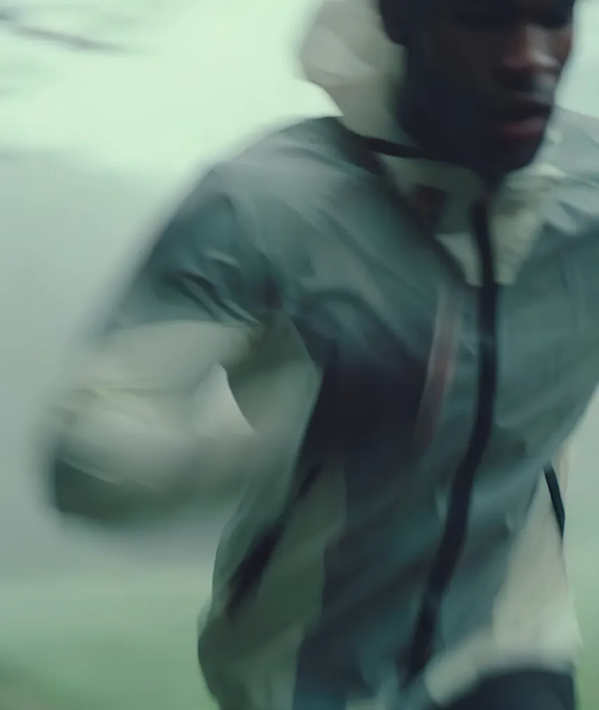 Blurred motion of a person running outdoors wearing a gray and white jacket with a hood.