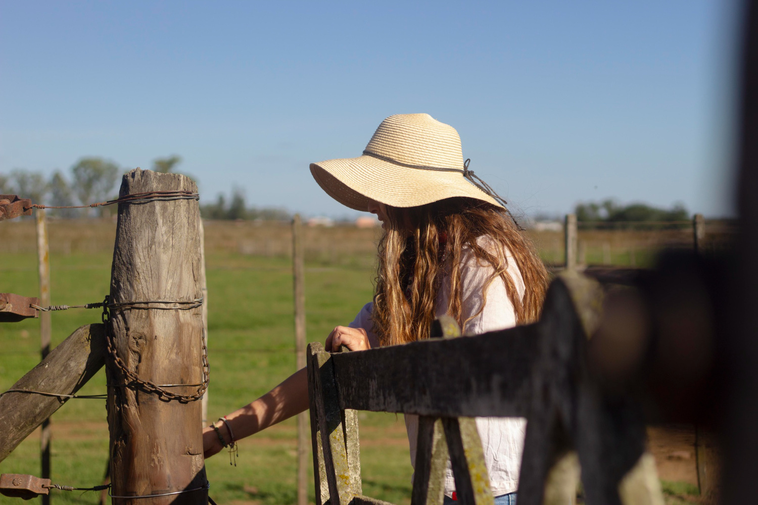 A woman in a wide-brimmed straw hat opening a farm gate onto the field