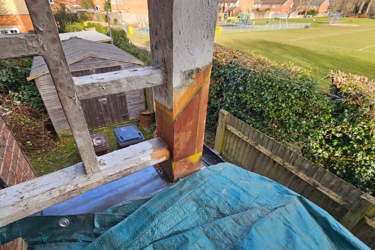 View from a balcony showing a wooden shed, green hedge, fence, and grassy playground with swings.