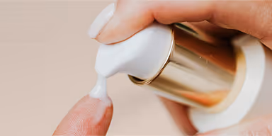Hand dispensing white cream from a gold and white pump bottle.