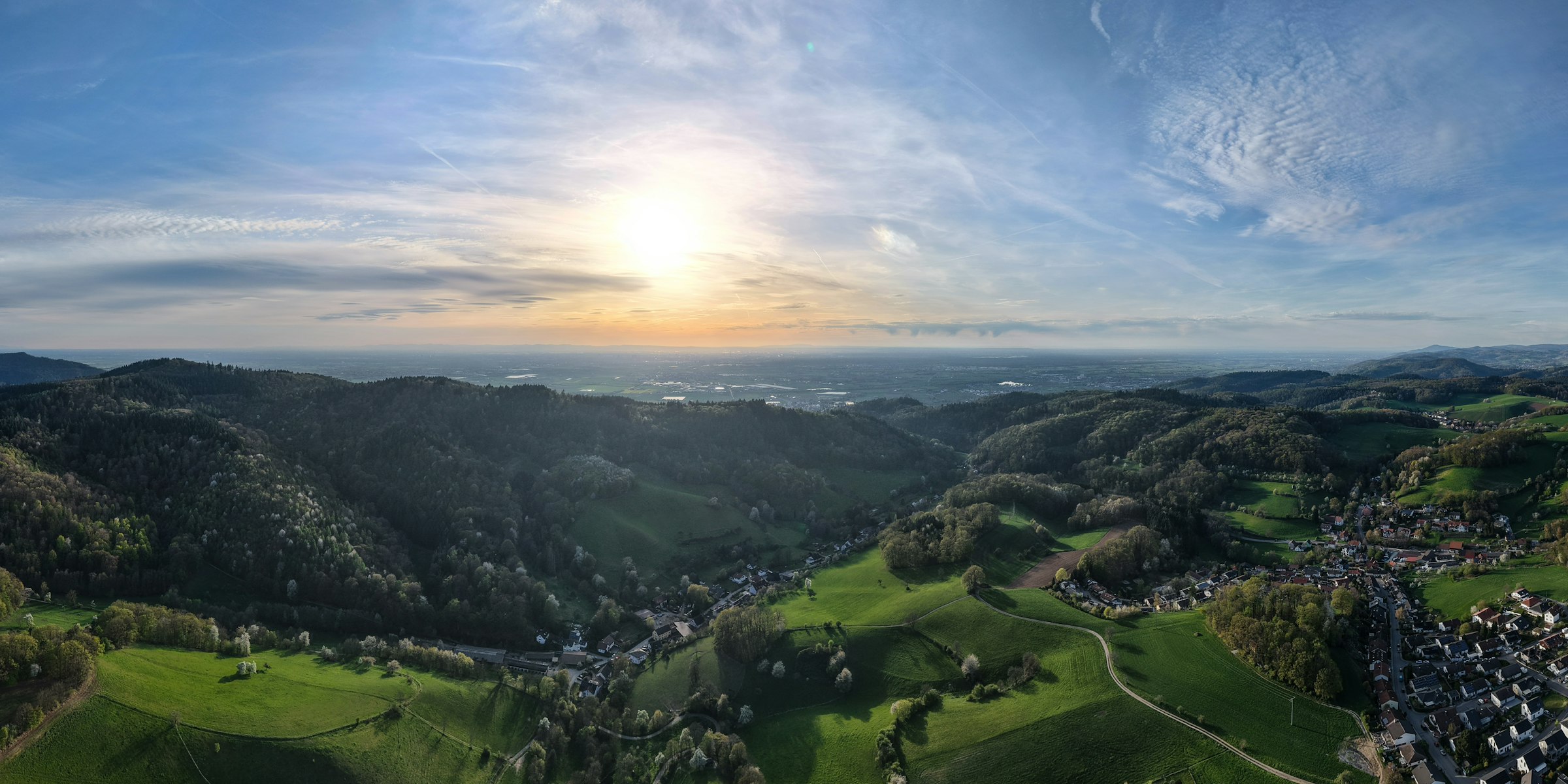 Sonnenbeschienene grüne Hügel mit kleiner Ortschaft im Allgäu, Symbolbild für den Bodenrichtwert von Grundstücken (Foto: Bernd Dittrich / Unsplash)