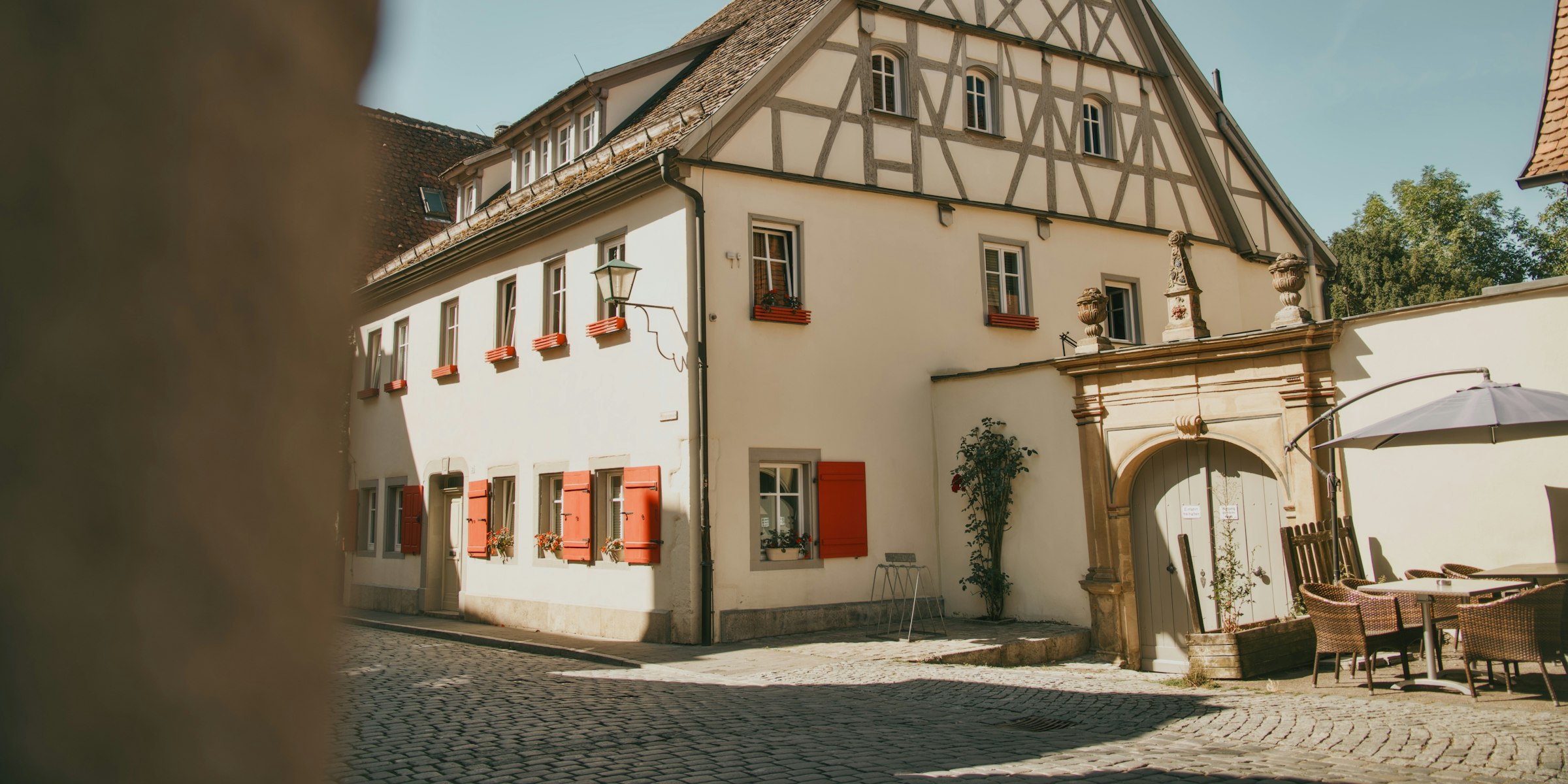 Altes Fachwerkhaus mit roten Fensterläden an einer Kopfsteinpflasterstraße, Symbolbild für eine geerbte Immobilie im Allgäu (Foto: Dawid Tkocz / Unsplash)