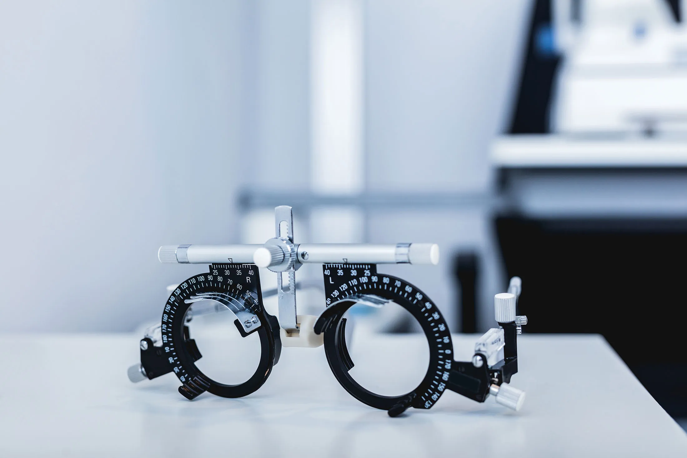 A pair of black and silver adjustable trial frames used for eye exams resting on a white surface in an optometrist's office.