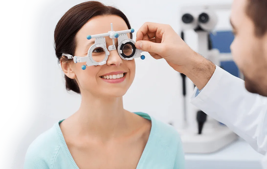 Woman smiling while an optometrist adjusts a trial frame on her face during an eye exam in a clinical setting.
