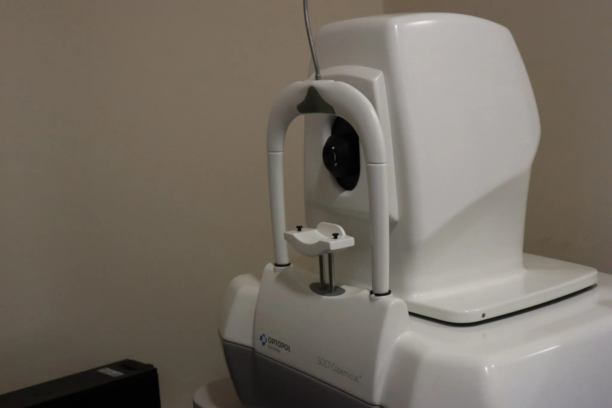 Optopol SOCT Copernicus ophthalmic imaging device used for eye examination against a plain beige wall.