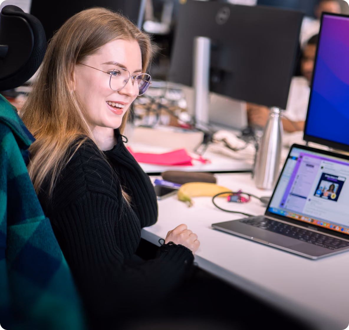 Woman smiling at her laptop in a busy office