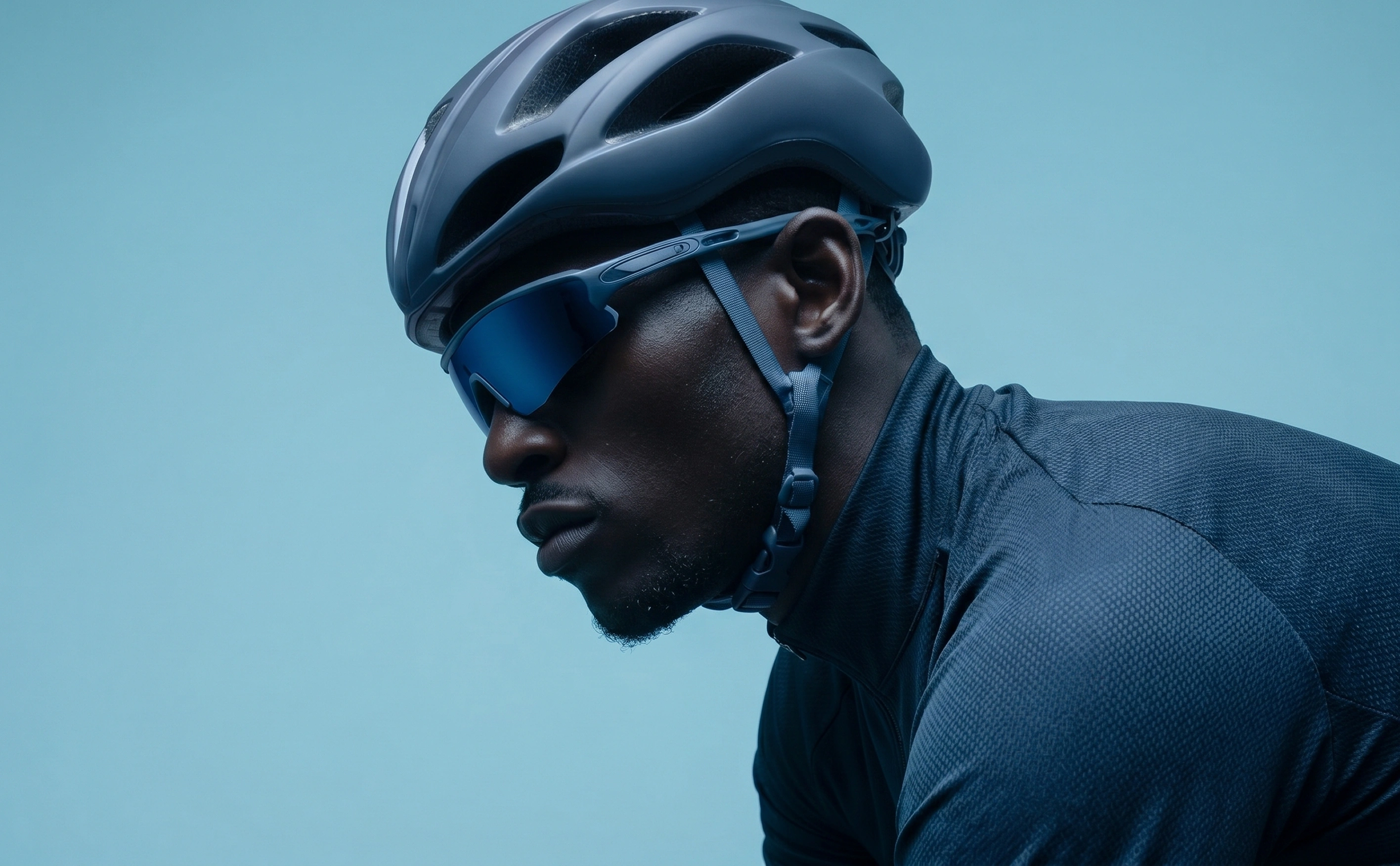 Profile of a cyclist wearing a blue helmet, blue sunglasses, and a blue cycling jersey.