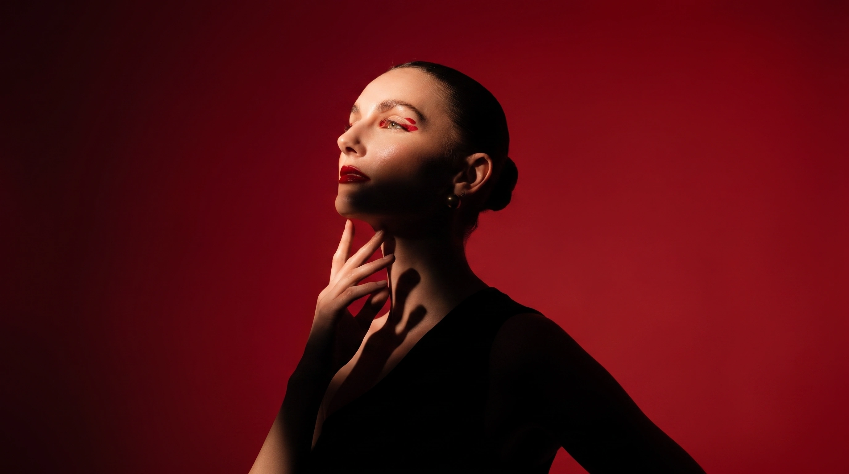 Woman with hair in a bun holding a pair of sunglasses, looking at them thoughtfully.