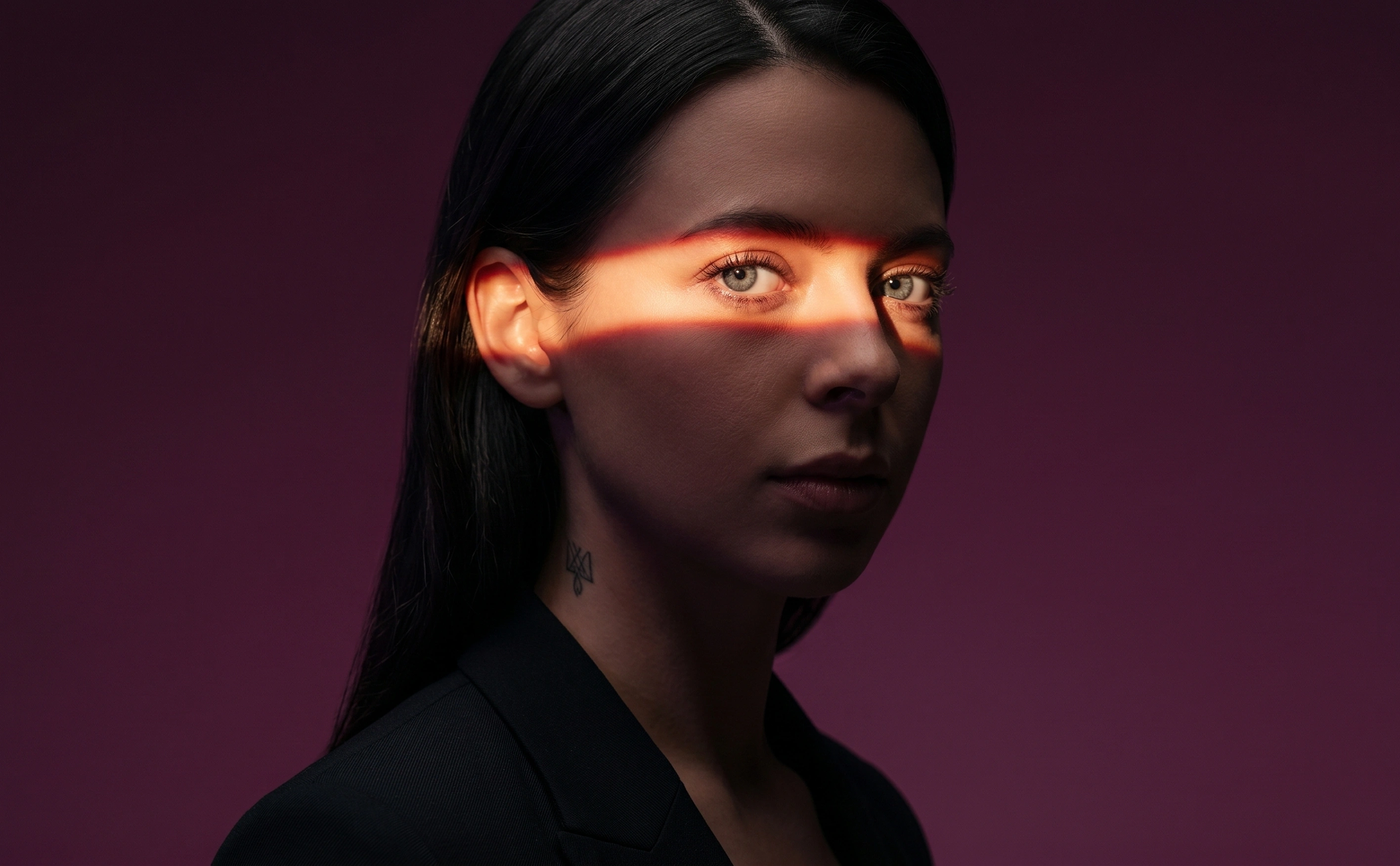 Woman with dark hair and tattoo on neck illuminated by a horizontal stripe of orange light across her eyes.