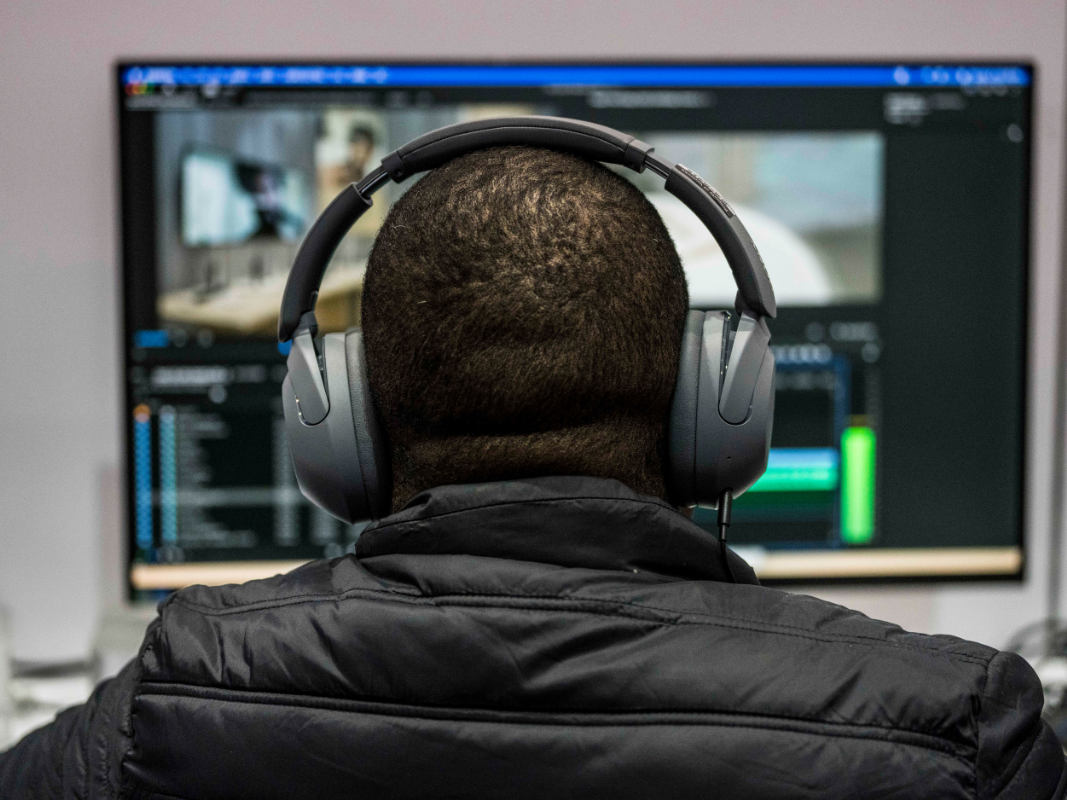 Person wearing headphones and a black jacket editing video on a computer screen.