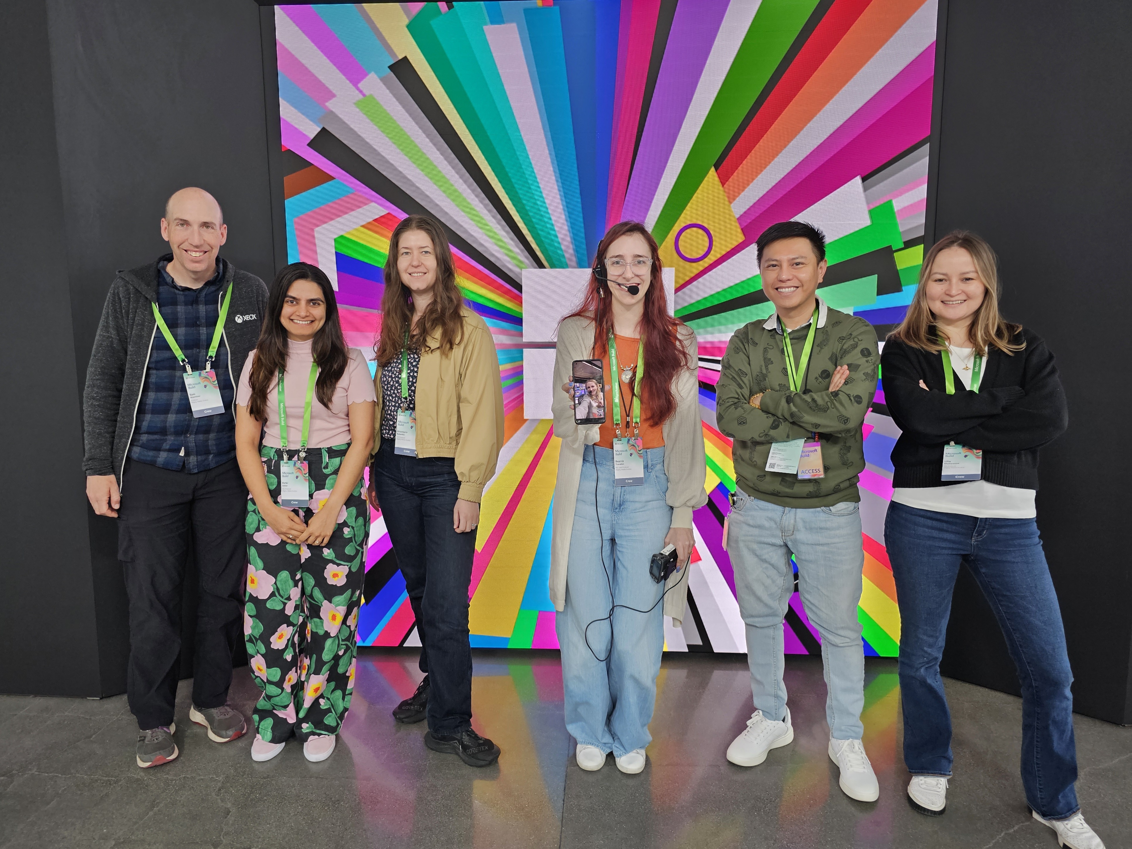 Group of six people standing smiling in front of a colorful abstract background.