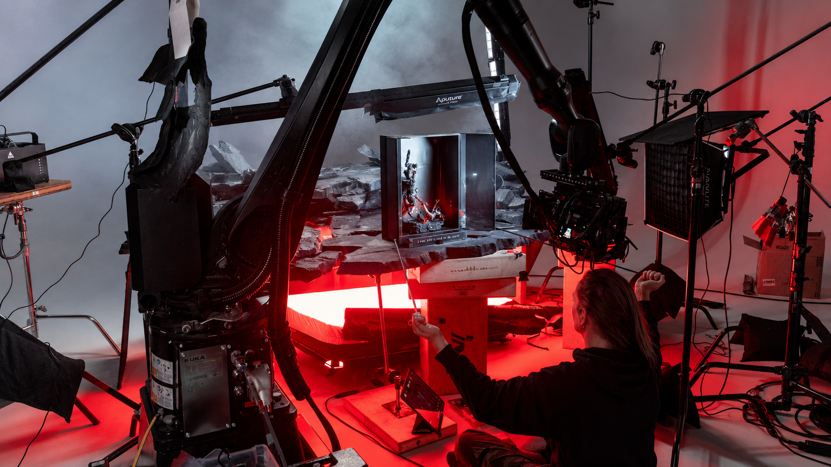 Person controlling robotic arm filming miniatures on a detailed set with red and blue lighting in a studio.