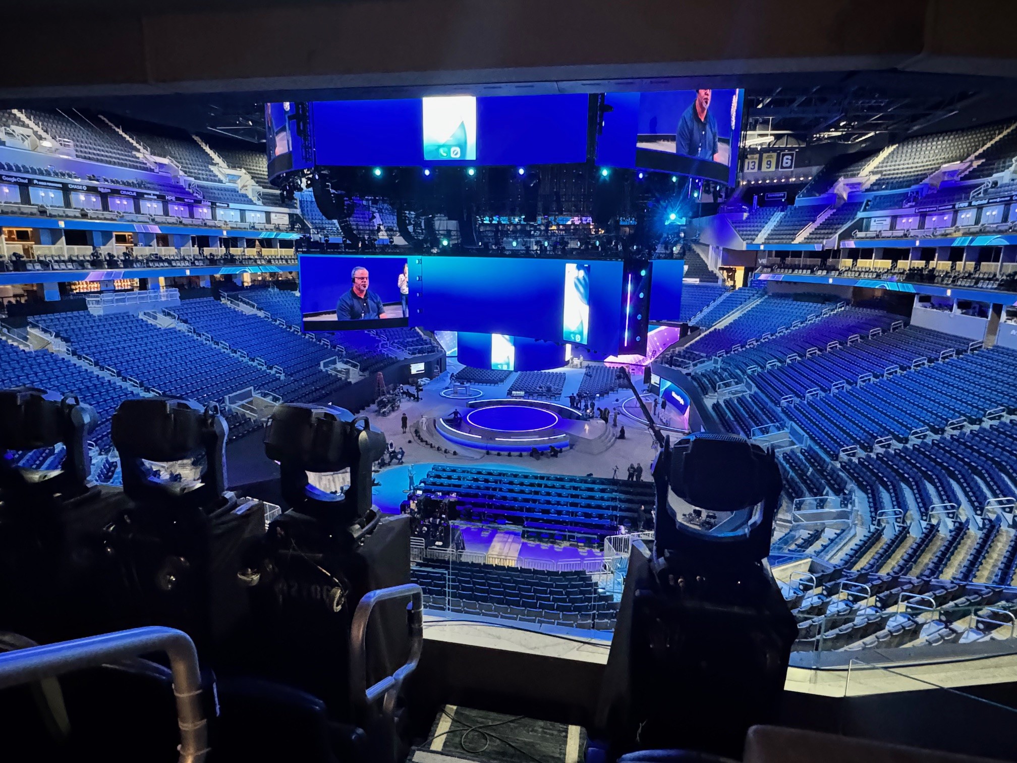 Empty arena with a circular stage, large video screens, and blue lighting before an event.