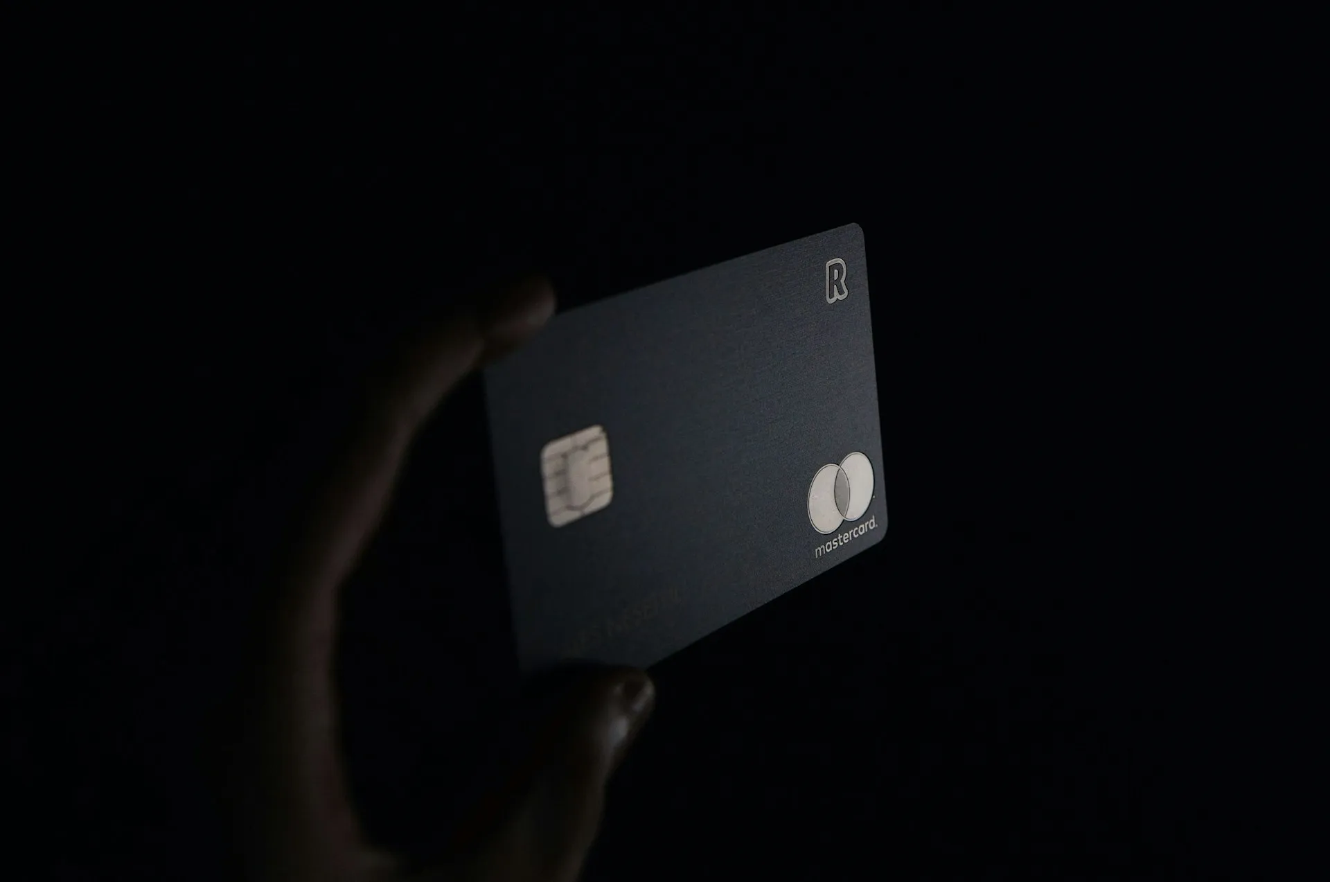 Hand holding a dark bank card against a black background
