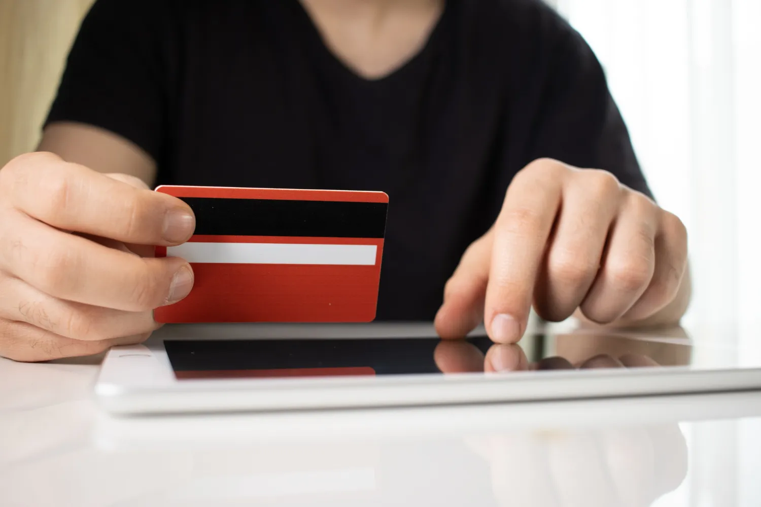 Hands holding a red bank card while shopping online on a tablet