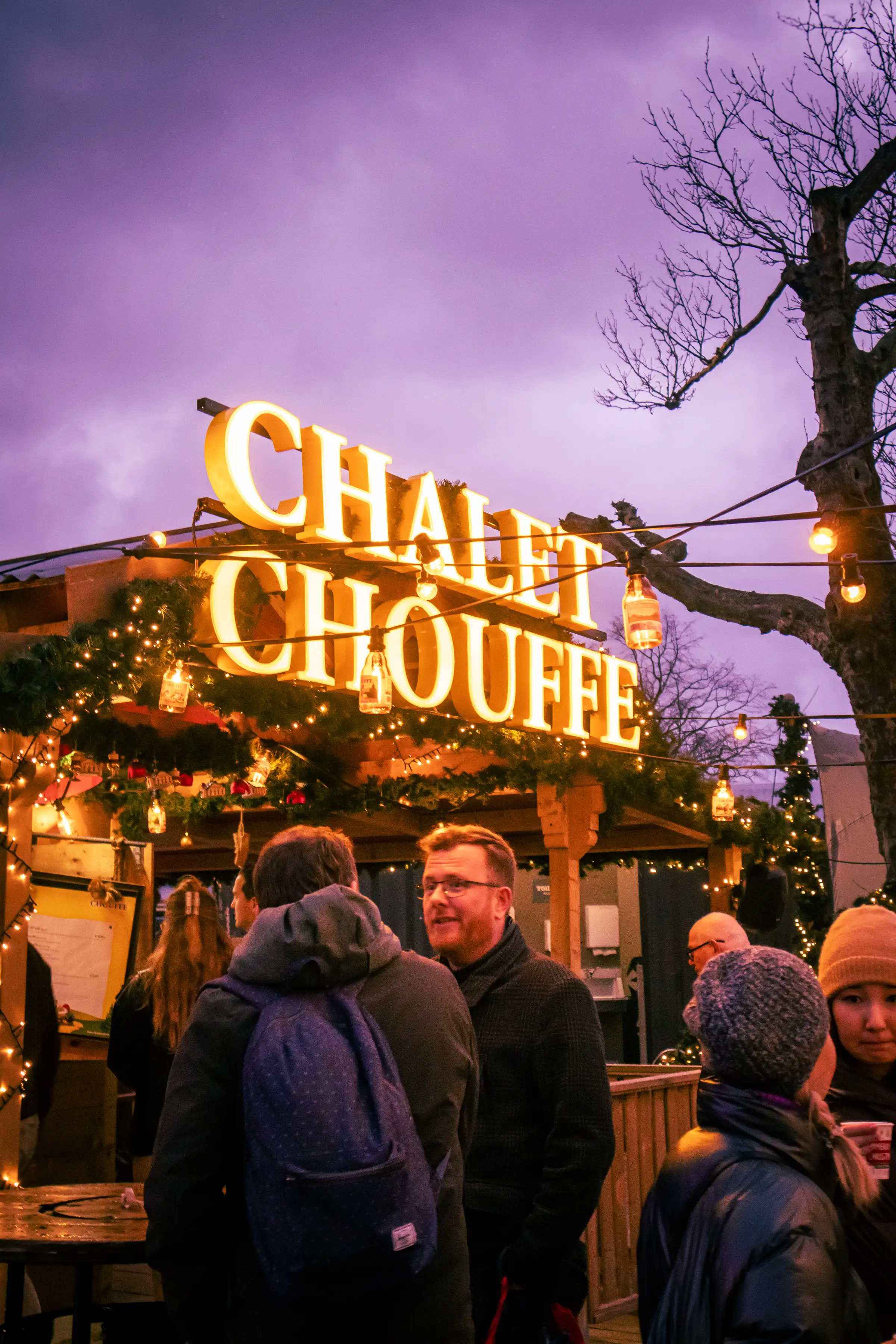 Black wooden house on top of a grassy hill under a pale sky.